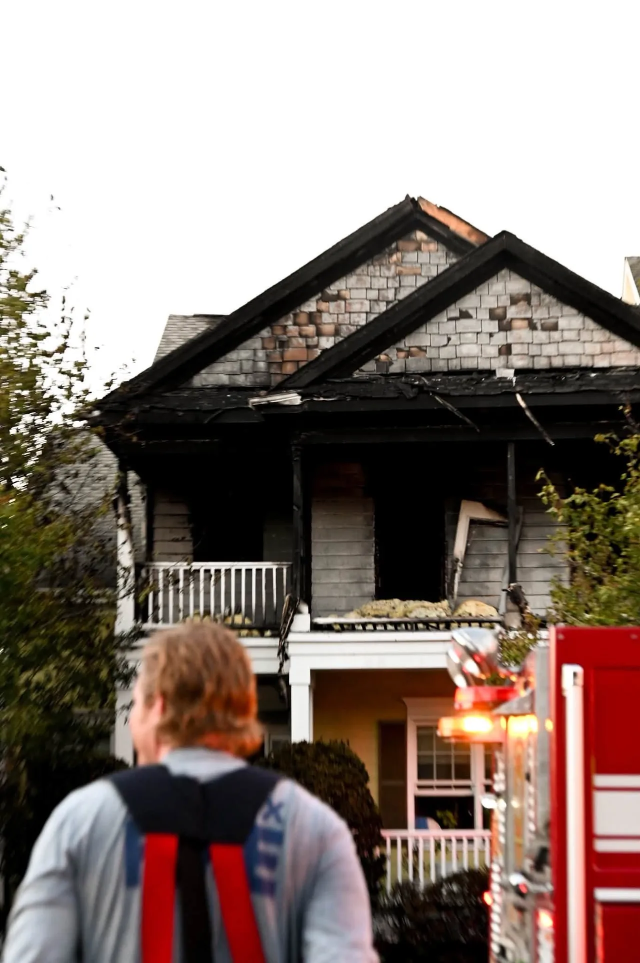 Fire damage to the second floor and roof of the Center Street home in Apex after the Oct. 6, 2026 fire, with a firefighter in the foreground.